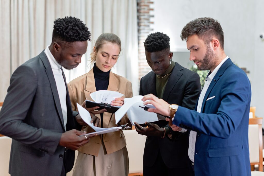 A diverse group of professionals in business attire reviewing documents in an indoor setting.